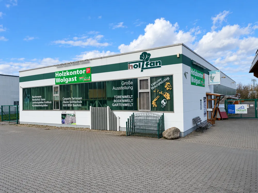 Gebäude des Holzkontors Wolgast mit beschrifteter Fensterfront und Zaunausstellung
