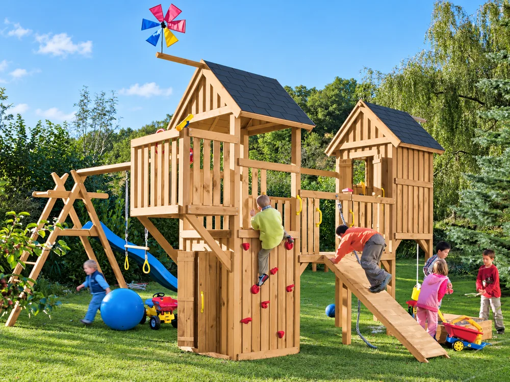 Kinder spielen auf einer Holzspielanlage mit Klettertürmen, Schaukel und Rutsche im Garten.