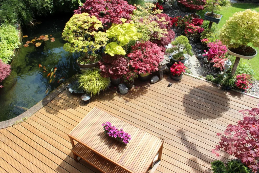 Holzterrasse mit Gartentisch neben einem Teich und farbenfroher Bepflanzung.